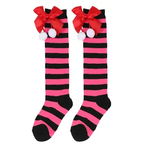 Close-up of pink and black striped knee-high socks with red bow and white pom-poms.