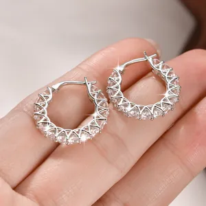 Primer plano macro de pendientes de aro plateados con diamantes sostenidos por los dedos
