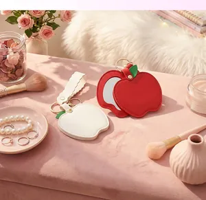 Detailed view of apple-shaped PU leather pocket mirrors with keychains on pink velvet