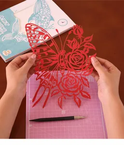 Gros plan d'un art de papier découpé papillon et rose rouge sur un tapis de découpe.