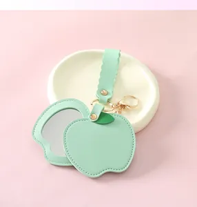 Detail showing mint green apple-shaped PU leather mirror keychain on a white tray.