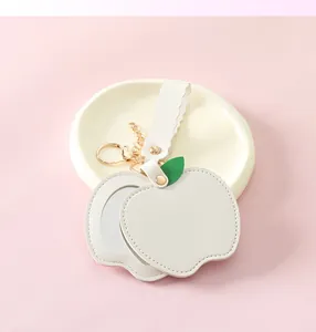 Detail view of cream white apple-shaped PU leather mirror keychain with gold hardware
