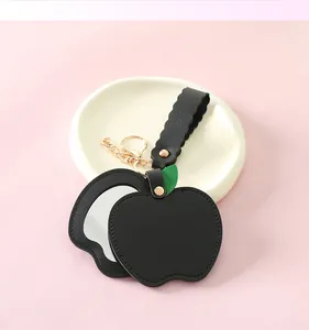 Detail view of black apple-shaped PU leather folding mirror keychain with gold ring