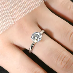 Gros plan d'une bague de fiançailles en moissanite de 2 carats sur main avec dentelle.
