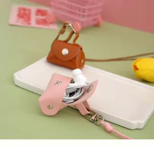 Detail view of a pink mini PU leather pouch holding wired earphones on a white tray.