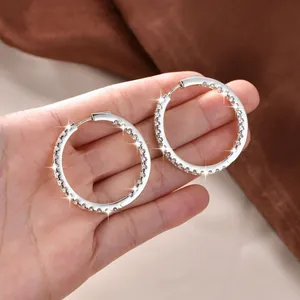 Detailaufnahme von silbernen Creolen mit glitzernden Kristallen in der Hand.