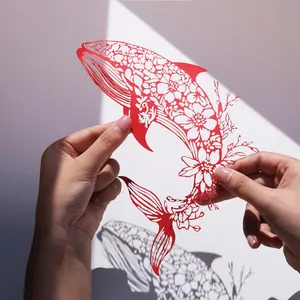 Art du papier découpé baleine rouge avec motifs floraux tenu à la main sur blanc