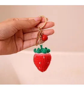 Handgemaakte gehaakte aardbei-sleutelhanger met belletje, detailopname van gebreide textuur.