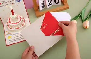 Close-up of hands placing a detailed 3D pop-up birthday cake card into its envelope