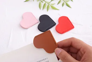 Close-up of a hand using a heart-shaped PU leather page corner bookmark on white paper.