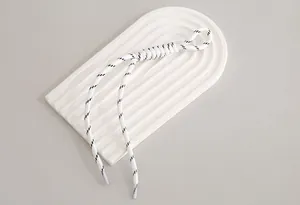 Close-up of a minimalist white and black braided nylon lanyard on a textured display tray