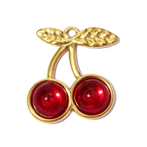 Close-up of a gold-plated stainless steel cherry pendant with red resin stones.