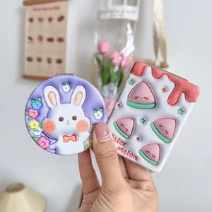 Macro view of cute cartoon folding compact mirrors featuring 3D embossed rabbit and watermelon designs.