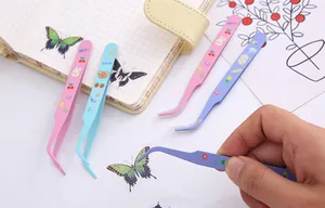 Close-up of a hand using a pastel purple tweezer to apply a butterfly sticker to a journal.