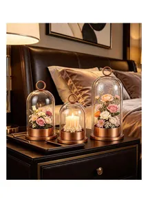 Trois dômes décoratifs en verre avec socles en cuivre et fleurs sur table de chevet.