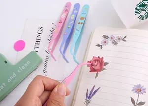 Close-up of a pink cartoon tweezer picking up a floral sticker in a scrapbook notebook