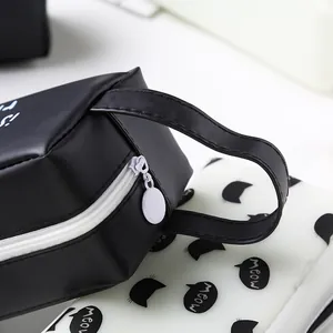 Détail d'une trousse noire en cuir PU avec fermeture éclair blanche et poignée.