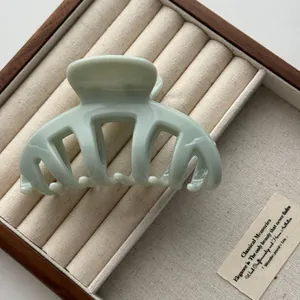 Detail of a sage green marble hair claw clip placed in a wooden jewelry box.
