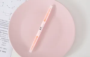 Detailed view of an orange dual-tip highlighter placed on a soft pink decorative plate