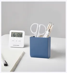 Detail view of a dark blue wall-mounted pen holder with stationery on a white desk