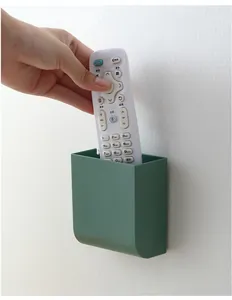 Wall-mounted green storage box holding a remote control on a plain white wall.