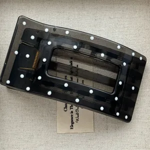 Close-up detail of a dark grey translucent polka dot hair claw clip on a neutral background