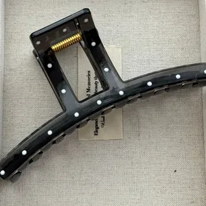 Detailed view of a black hair claw clip with white polka dots on a linen background