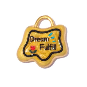 Macro view of a yellow stainless steel charm featuring Dream Fulfill text and a rose