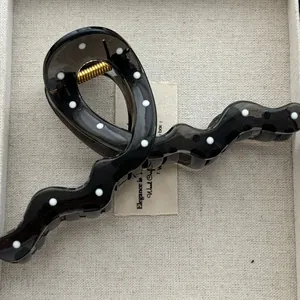 Detailed view of a glossy black wave hair claw clip with elegant white polka dots.