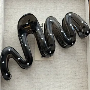 Close-up of a black translucent wavy hair claw clip with white polka dots