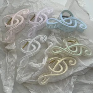 Matte Haarklammern in Notenform in Pastellfarben auf weißem, strukturiertem Papier.