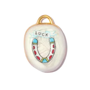 Detail view of a white enamel horseshoe charm featuring 'LUCK' text with gold-tone rim