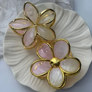 Close-up of marbled resin plumeria hair claws with elegant gold-plated metallic frame