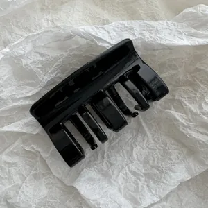 Primer plano de una pinza para el cabello negra brillante sobre fondo blanco de papel
