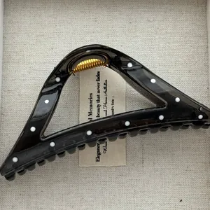 Detail of black triangular hair claw clip with white polka dots and gold spring