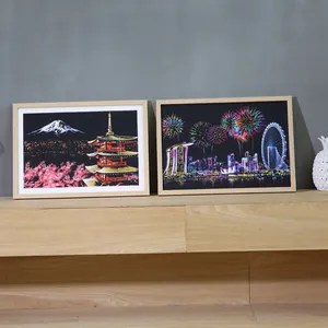 Two wooden frames displaying city night scratch art on a minimalist wooden shelf.