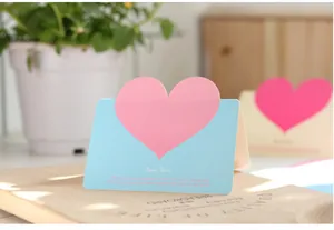 Dettaglio di un biglietto d'auguri azzurro con un grande cuore rosa a rilievo in primo piano.