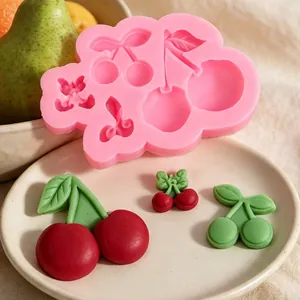 Detail van roze kersen siliconen vorm met afgewerkte rode fondant decoraties op bord.