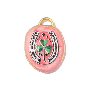 Close-up of pink stainless steel pendant featuring horseshoe and green clover designs.