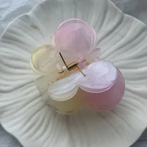 Close-up of gradient pink and yellow plumeria flower hair claw clip with gold spring detail.