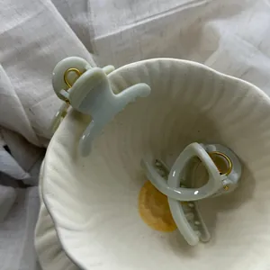 Minimalist mint green hair claw clips in a white ceramic bowl for elegant styling.