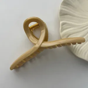 Detail view of a large minimalist beige hair claw clip with a glossy finish and gold spring