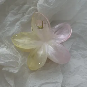 Close-up of a gradient pink and yellow plumeria flower hair claw clip on paper