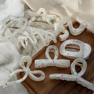 Collection of pearly white hair claw clips decorated with colorful rhinestones on wood