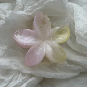 Detailweergave van een roze en gele plumeria bloem haarklem met een glanzende jelly finish.
