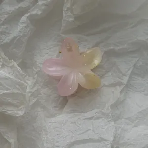 Close-up of small gradient plumeria flower hair claw clip on white textured background.