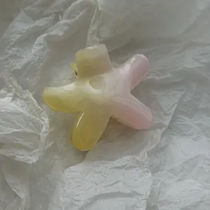 Close-up of a flower-shaped hair claw clip with pink and yellow gradient on tissue paper.
