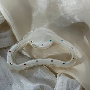 Detail of a cream marble hair claw clip with colorful rhinestone accents on silk fabric.