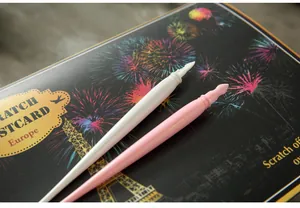 Close-up detail of white and pink plastic scratch art pens on a night city postcard