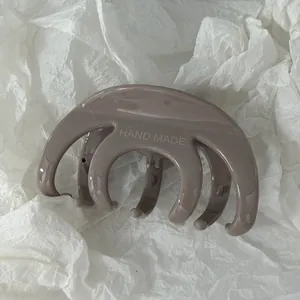 Dettaglio di un fermaglio per capelli taupe lucido su carta bianca strutturata.